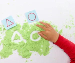 child tracing shapes in sand